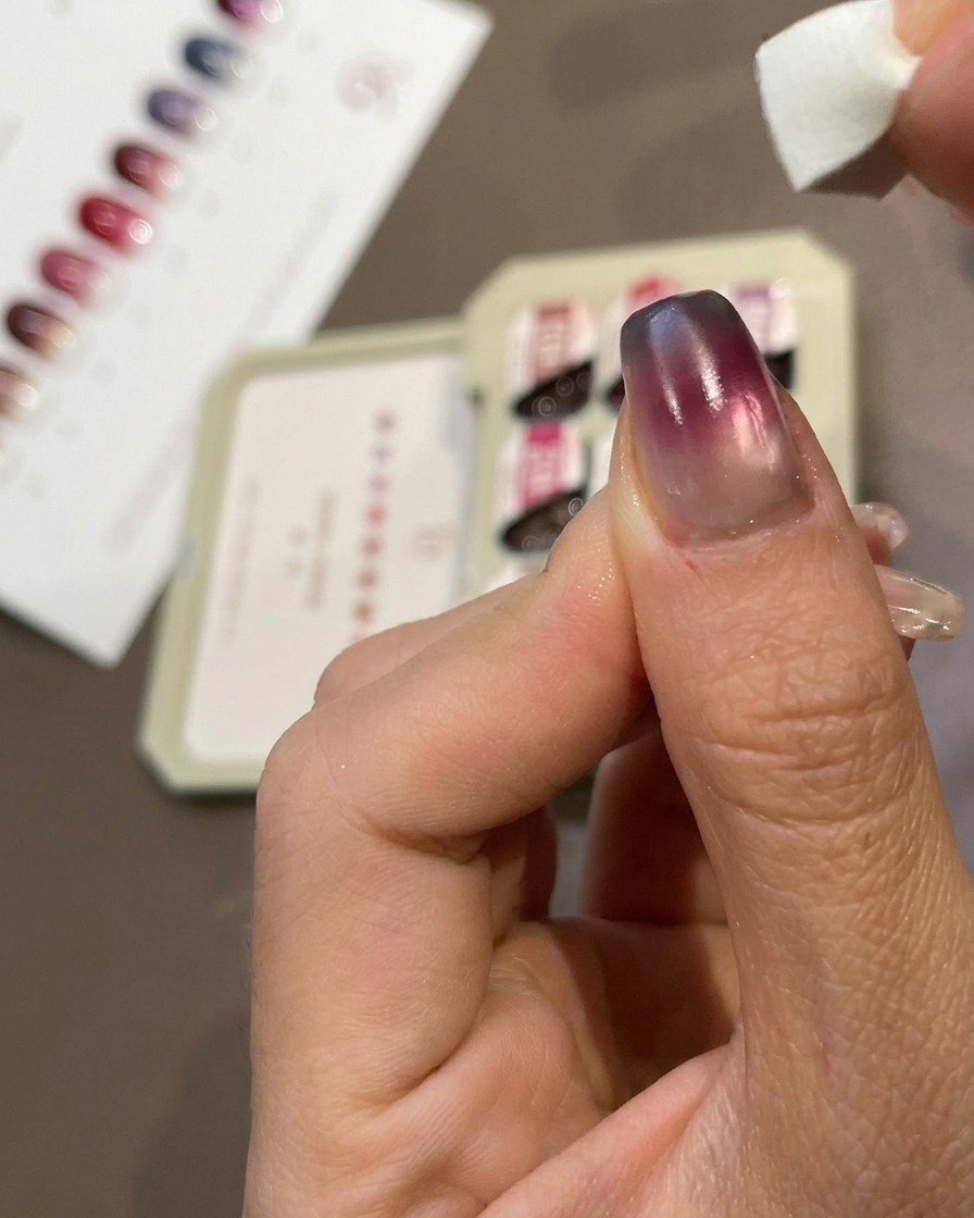 Primer plano de un dedo mostrando una pequeña esponja de maquillaje aplicando gel azul en la punta de una uña.