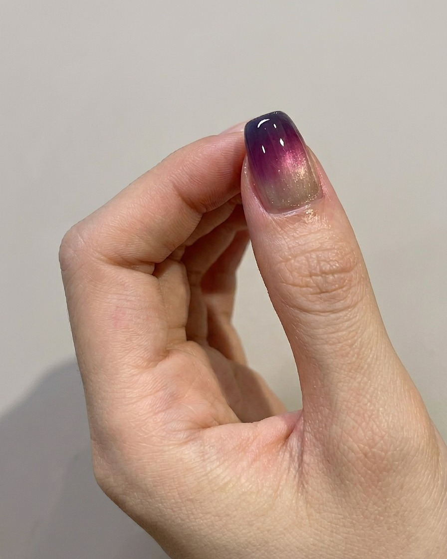 Un pincel aplicando una capa final de top coat brillante sobre un diseño de uñas ombré azul y morado.