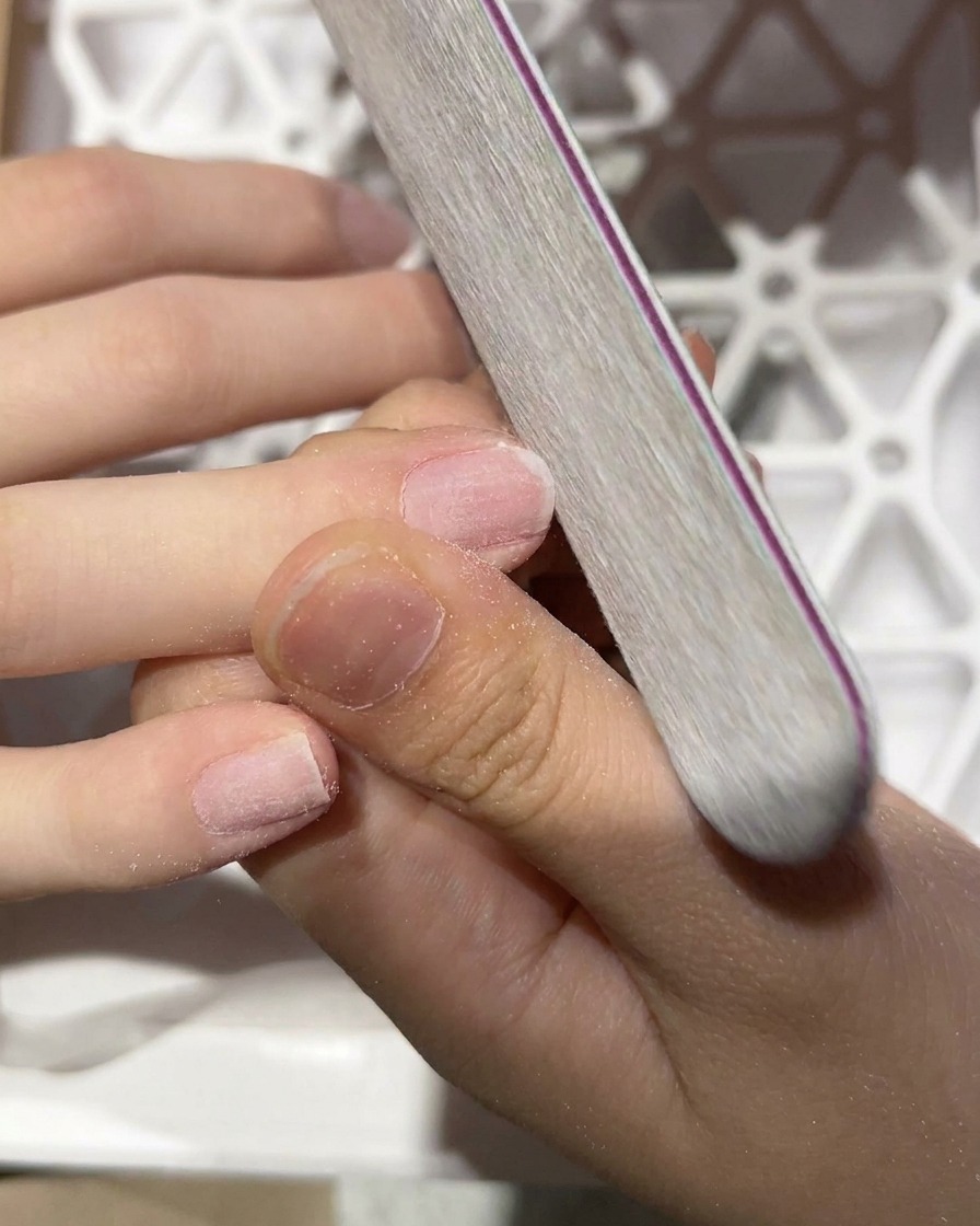 Primer plano de una lima manual puliendo la superficie de una uña natural.