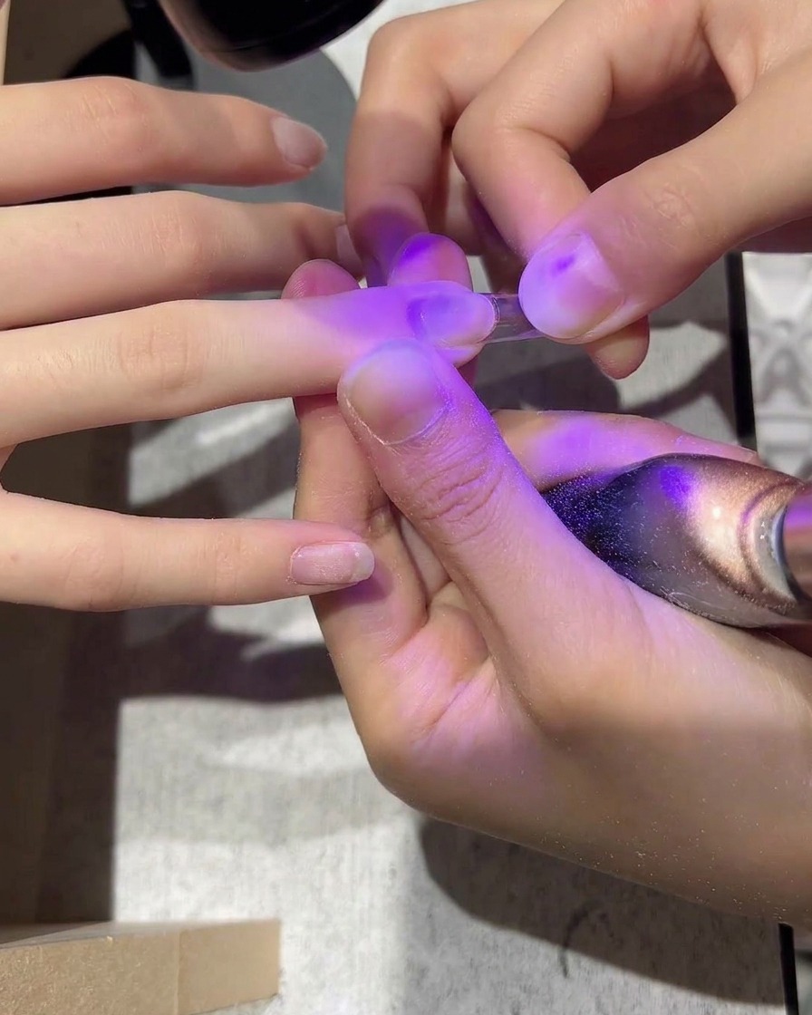 Un tip de uña de plástico transparente siendo aplicado sobre una uña natural con adhesivo.