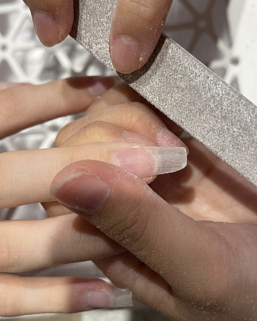 Primer plano de una lima manual dándole forma de almendra al borde libre de una extensión artificial.