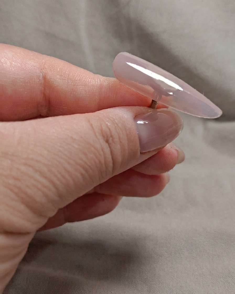 Un pincel aplicando una segunda capa de gel rosa nude translúcido en la uña.