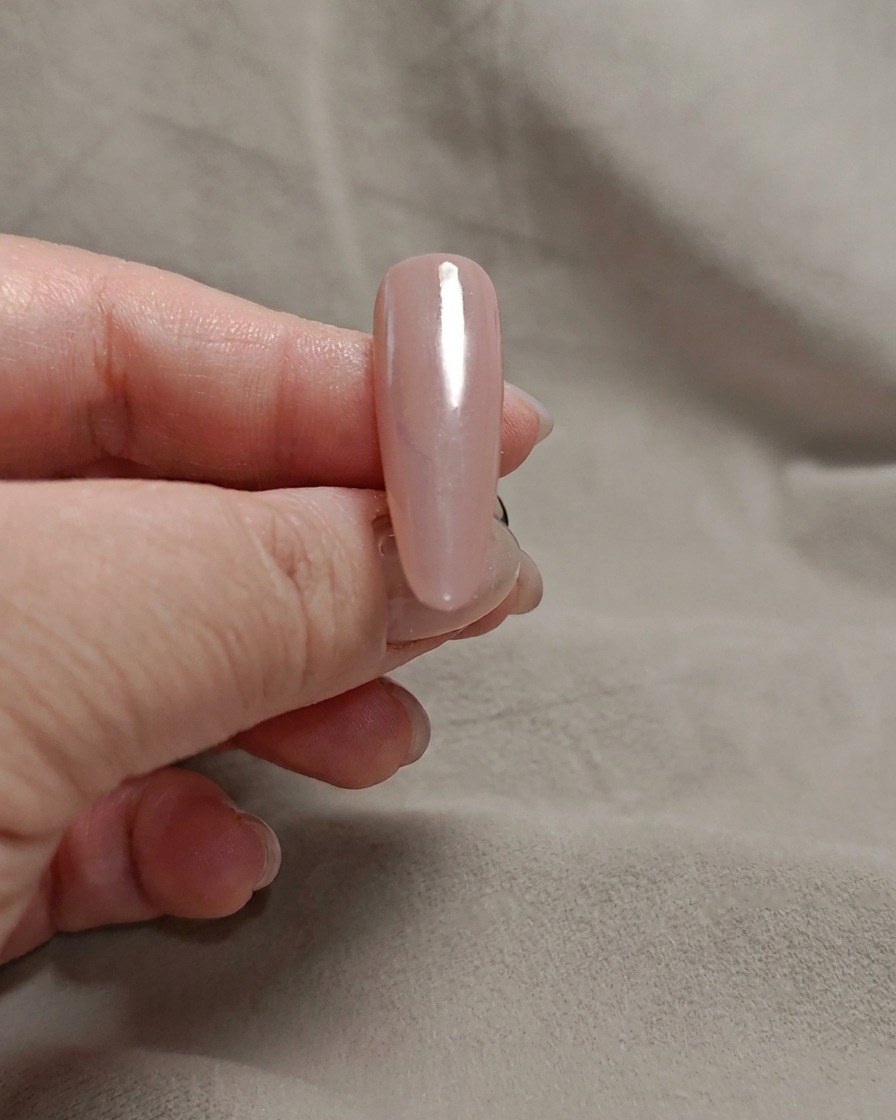 Una esponja de maquillaje aplicando gel blanco milky en la punta de una uña rosa.