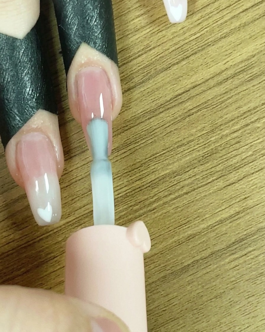 Un pincel aplicando una línea de esmalte de gel blanco en la punta de la uña.