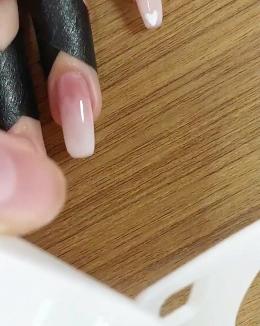 Una mano dentro de una lámpara UV/LED curando el diseño de uñas en degradado.