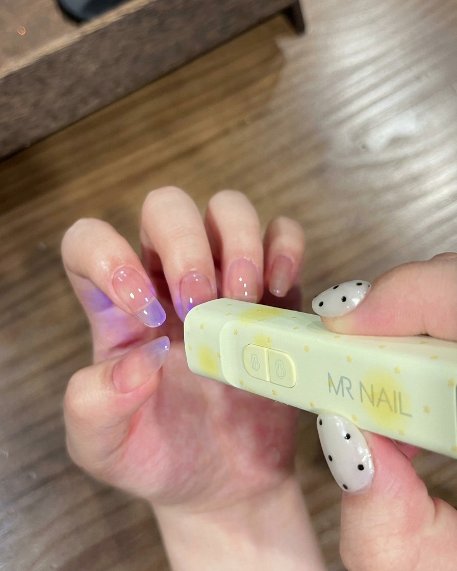 Uñas colocadas bajo una pequeña lámpara UV portátil de la marca MR NAIL para el curado.