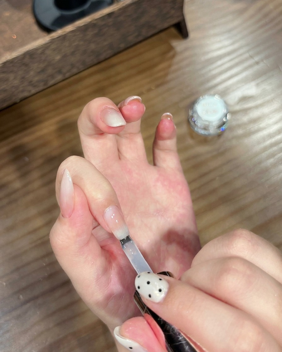 Un pincel aplicando un top coat transparente sobre una uña terminada con degradado y efecto cromado.