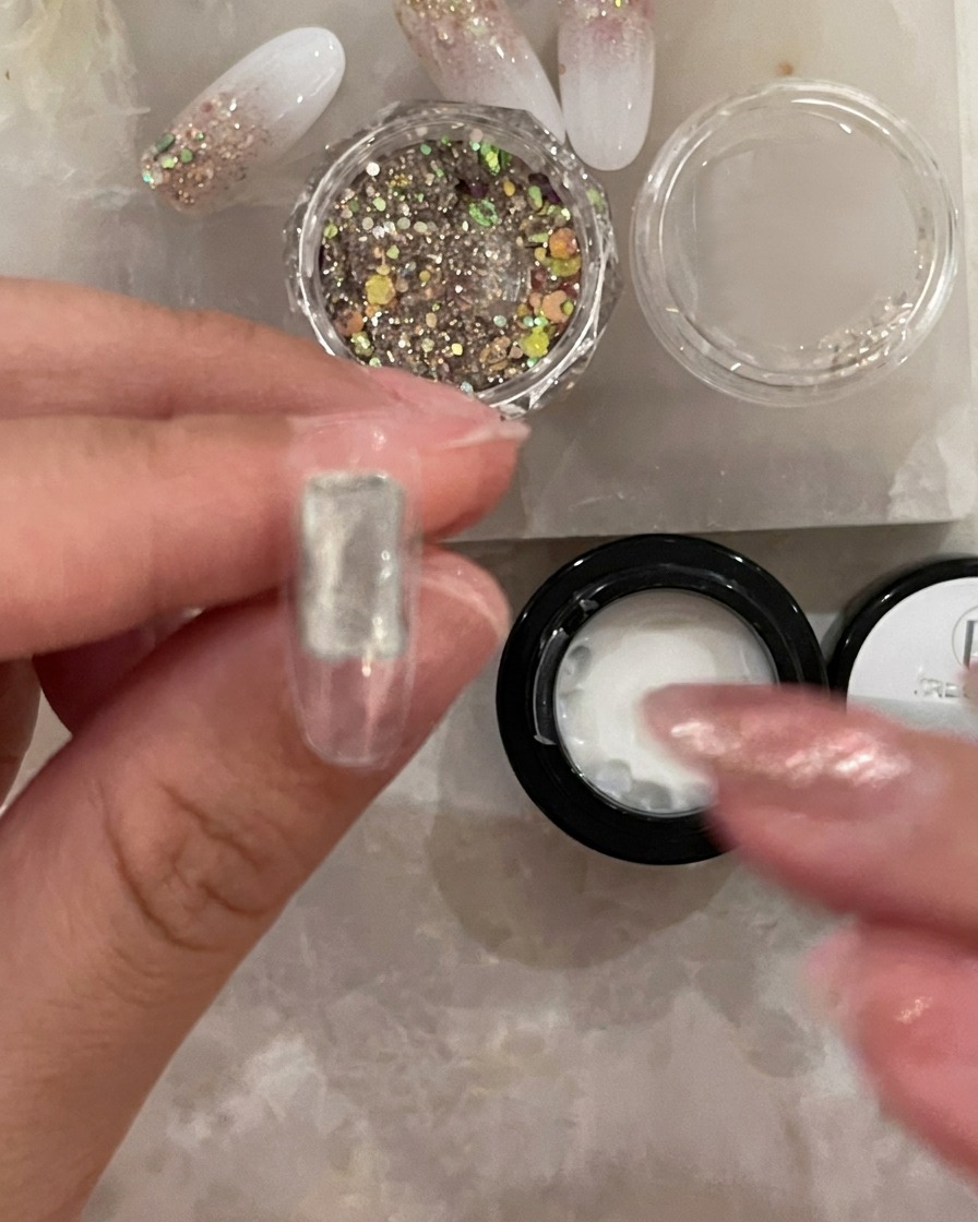 Un pincel pequeño aplicando una capa transparente y fina de base coat en el centro de un tip de uña artificial.