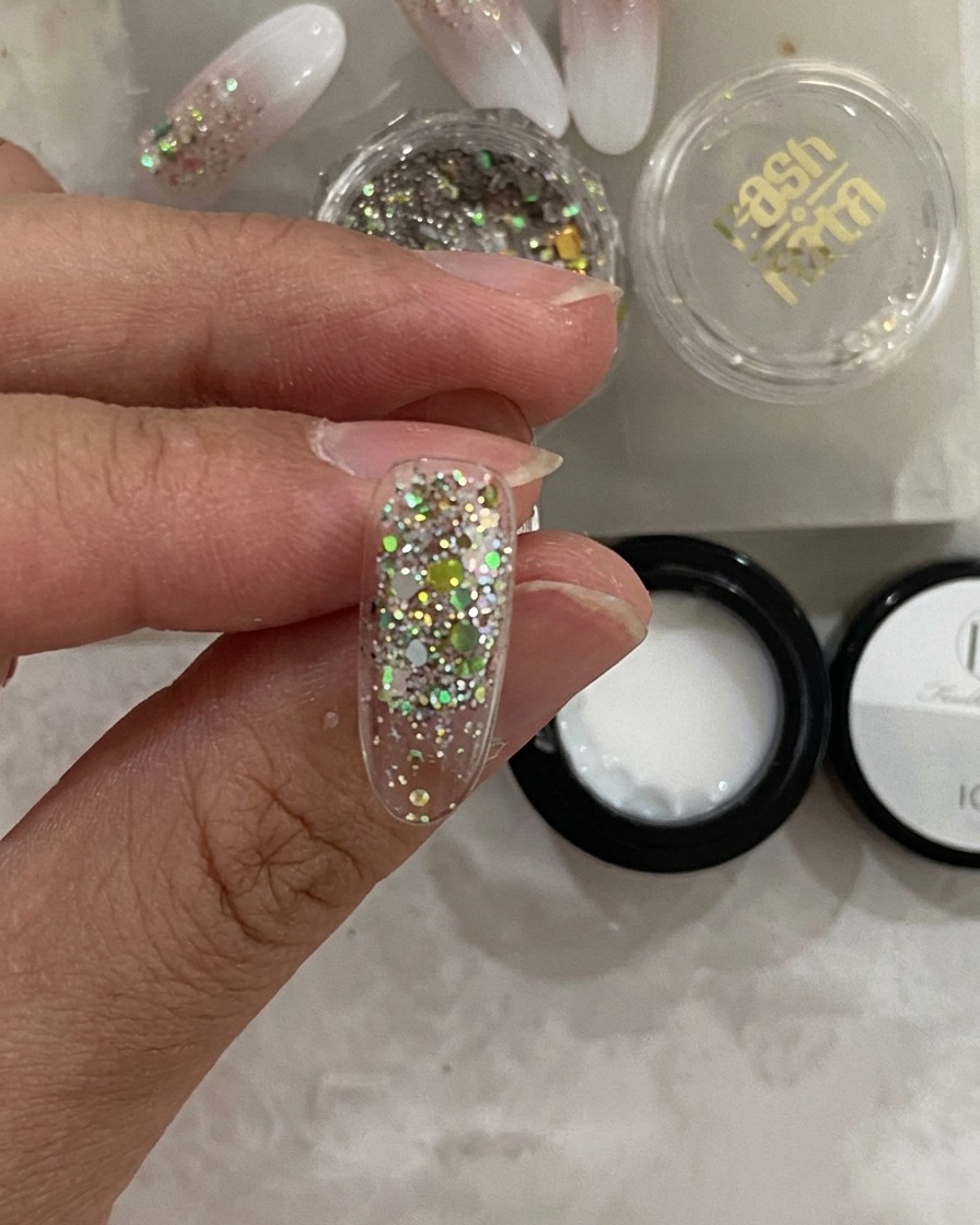 Vista en primer plano de un tip de uña dentro de una lámpara UV, con la capa de glitter ya fijada.