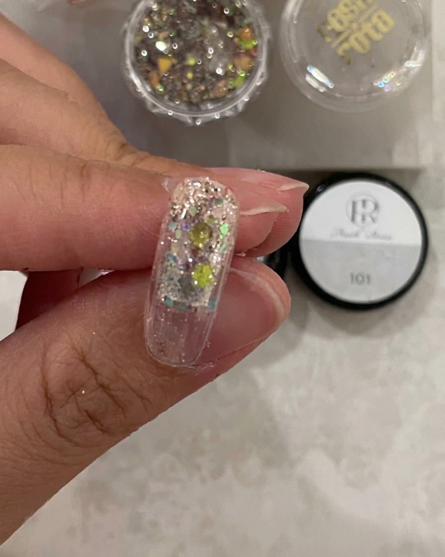 Primer plano de un tip de uña bajo la luz de curado, mostrando el gel de estructura fijado sobre el glitter.