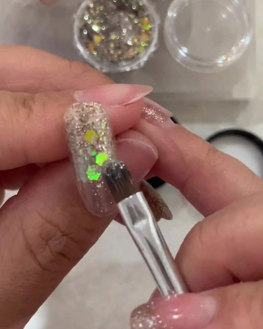 Un pincel aplicando una capa fina de gel blanco traslúcido en la punta de la uña, difuminando hacia el área de la cutícula con glitter.