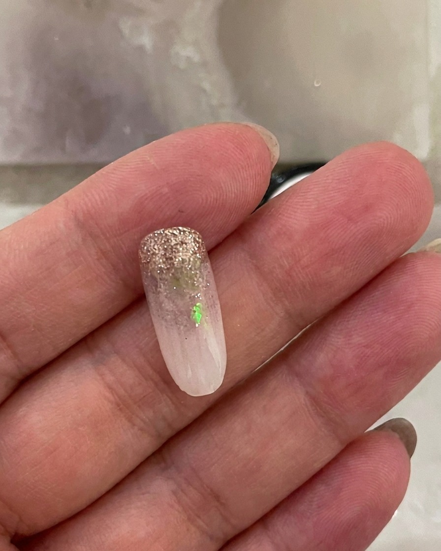 Una uña con el degradado blanco lechoso aplicado, reposando dentro de una lámpara de uñas UV mientras la luz está activa.