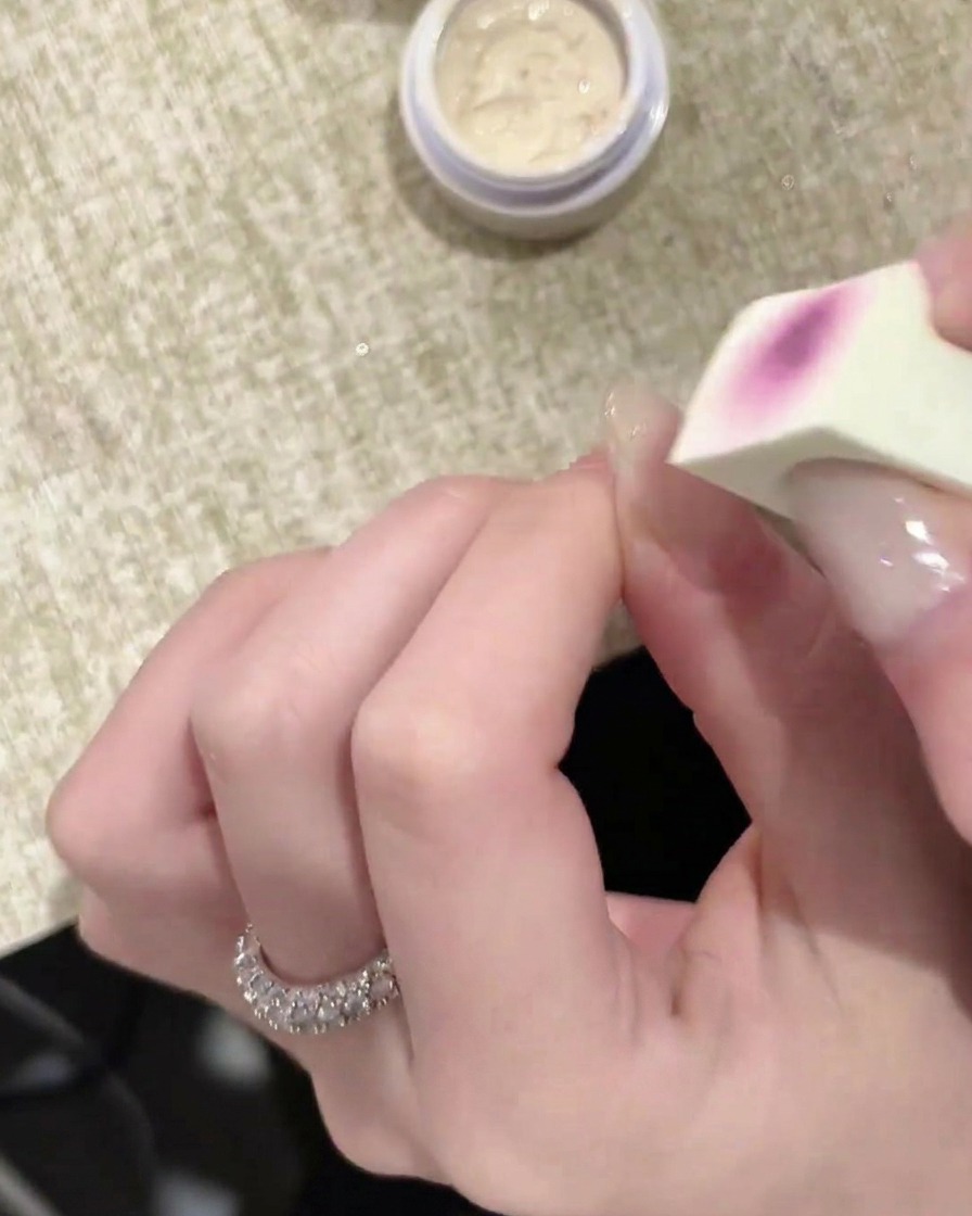 Primer plano de un aplicador de esponja aplicando una capa de gel blanco sobre una uña.