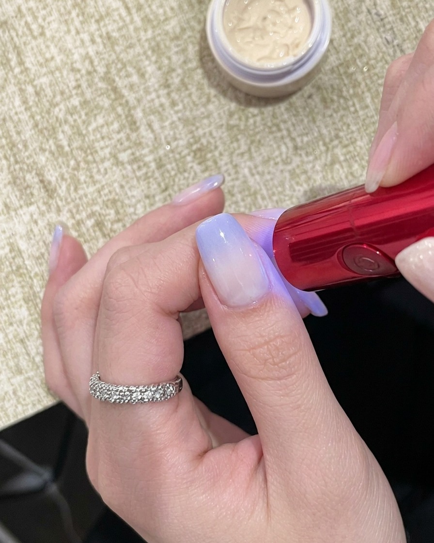 Una mano colocada bajo una lámpara UV portátil roja con las uñas visibles debajo.
