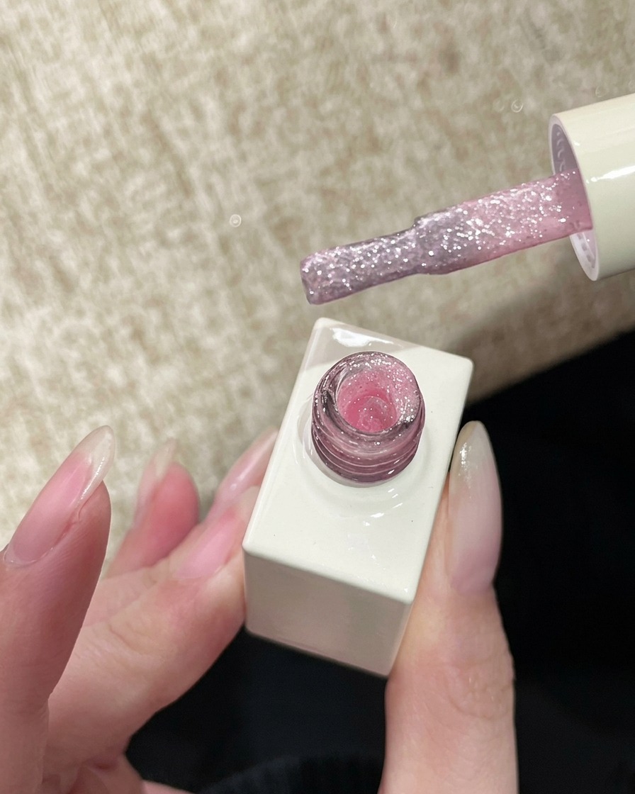 Un pincel de uñas sosteniendo gel de glitter rosa, listo para ser aplicado en la uña.