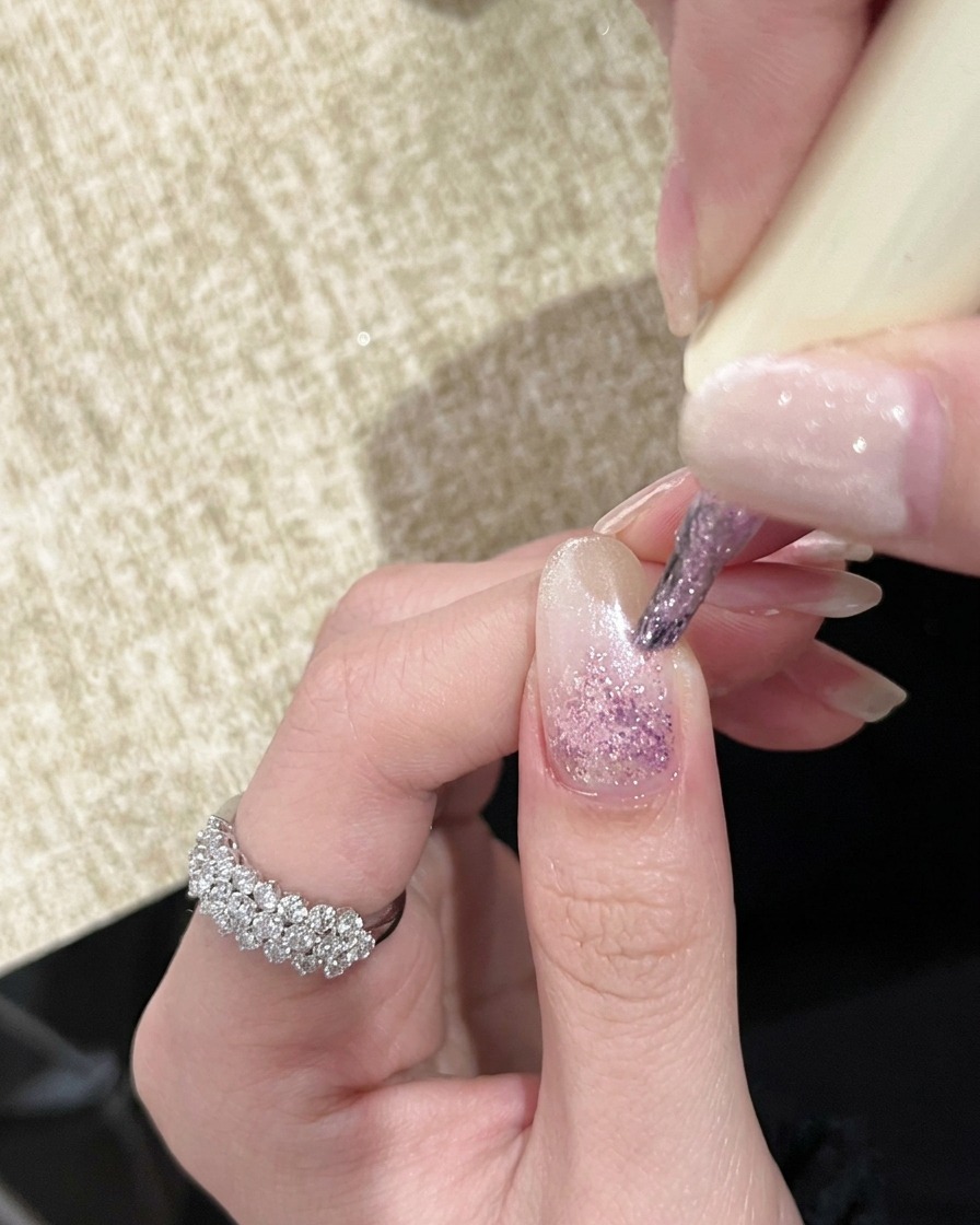 Una mano bajo una lámpara UV portátil con las uñas mostrando un efecto de degradado rosa claro.