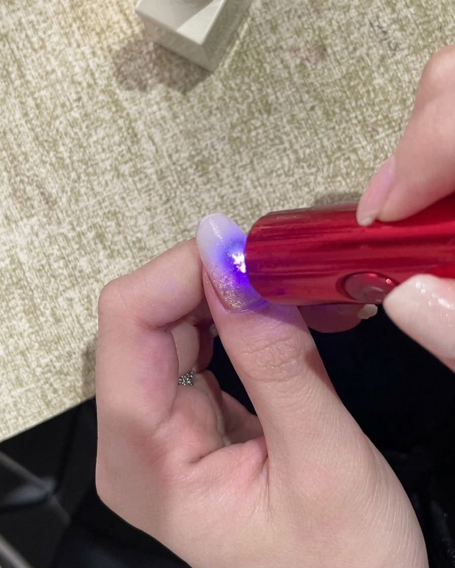 Una mano bajo una lámpara UV portátil, con la superficie de la uña brillando bajo la luz.