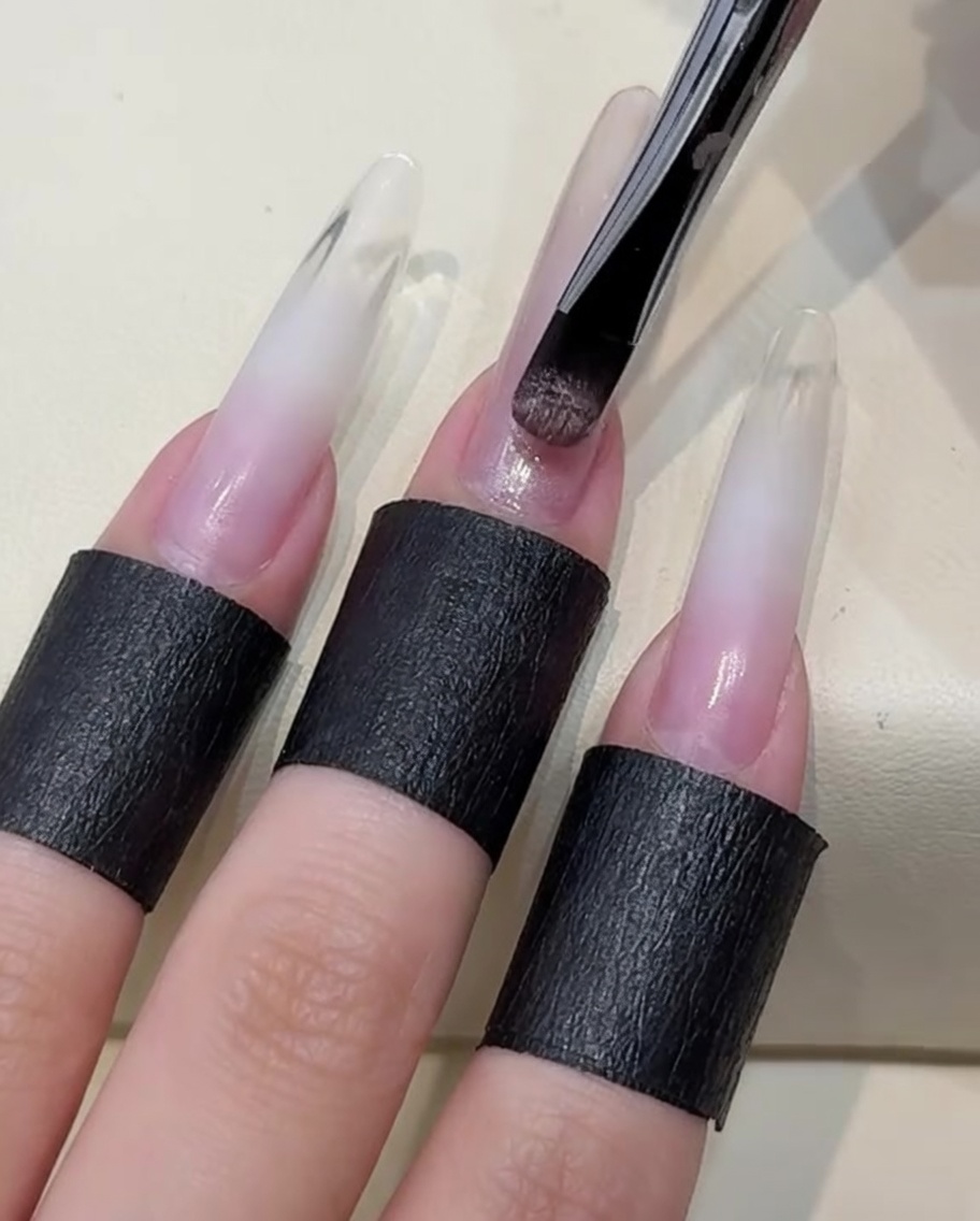Un pincel aplicando una capa de esmalte de gel cat-eye color nude claro sobre la uña.