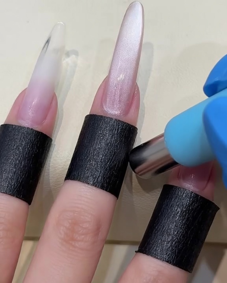 Un imán cilíndrico siendo sostenido cerca de una uña pintada con gel húmedo para desplazar las partículas magnéticas.