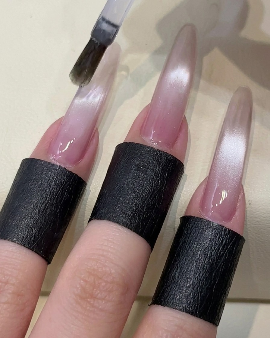 Un pincel aplicando un top coat transparente sin capa de inhibición sobre la uña de gel cat-eye.