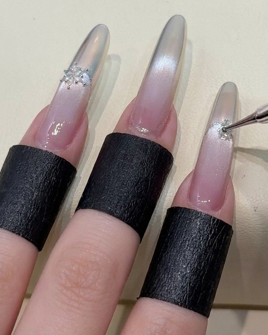 Un dedo índice siendo decorado con un cristal de copo de nieve, resaltando el proceso detallado del arte de uñas.