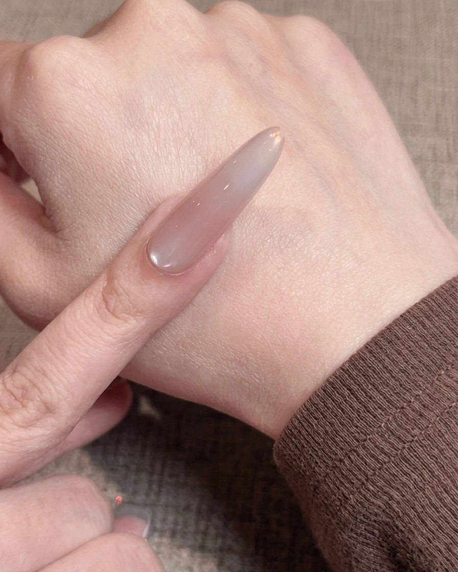 Primer plano de un pincel aplicando una capa fina y lisa de esmalte de gel nude sobre una uña preparada.