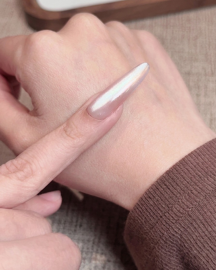 Un pincel de uñas aplicando un top coat rosa traslúcido sobre una uña con degradado, preparándola para el curado final.