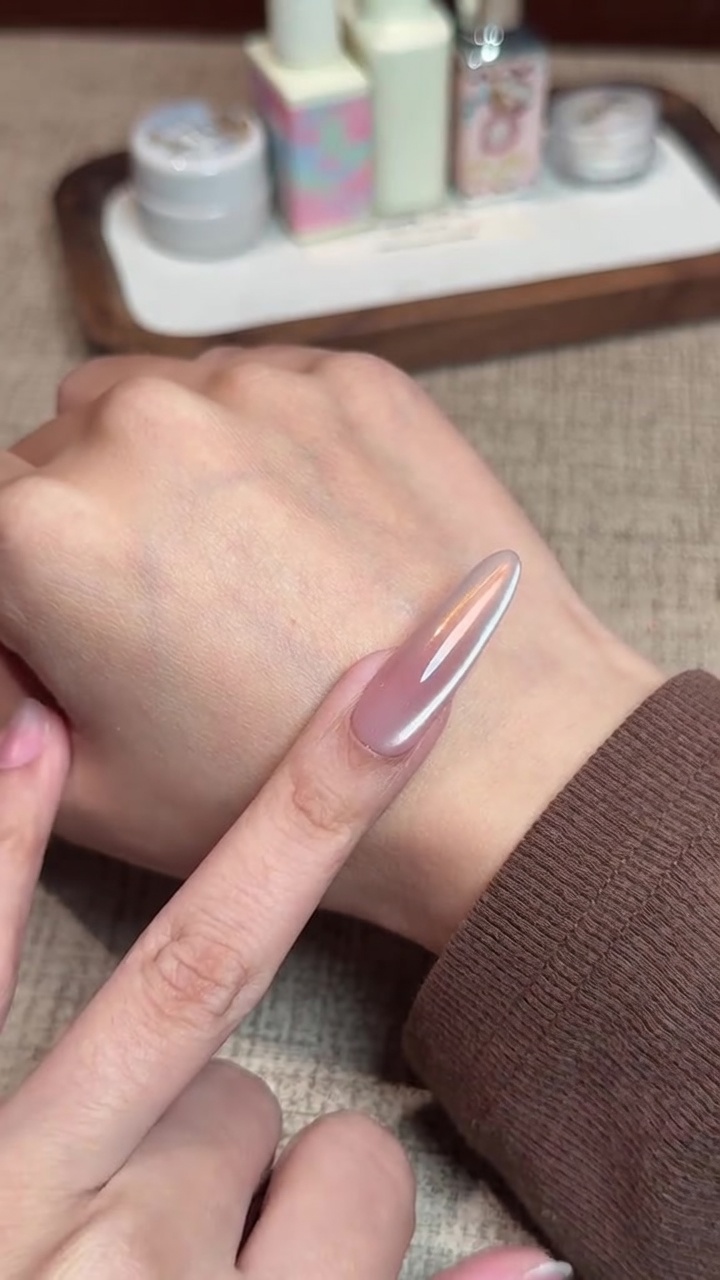 Primer plano de una uña larga almendrada con un acabado cromo aurora iridiscente sobre base degradada rosa, con un sutil reflejo magnético lateral.
