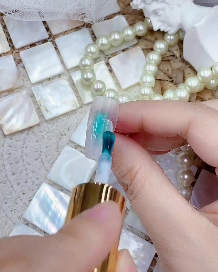 Un pincel aplicando una capa de esmalte de gel blanco lechoso sobre una punta de uña press-on transparente.
