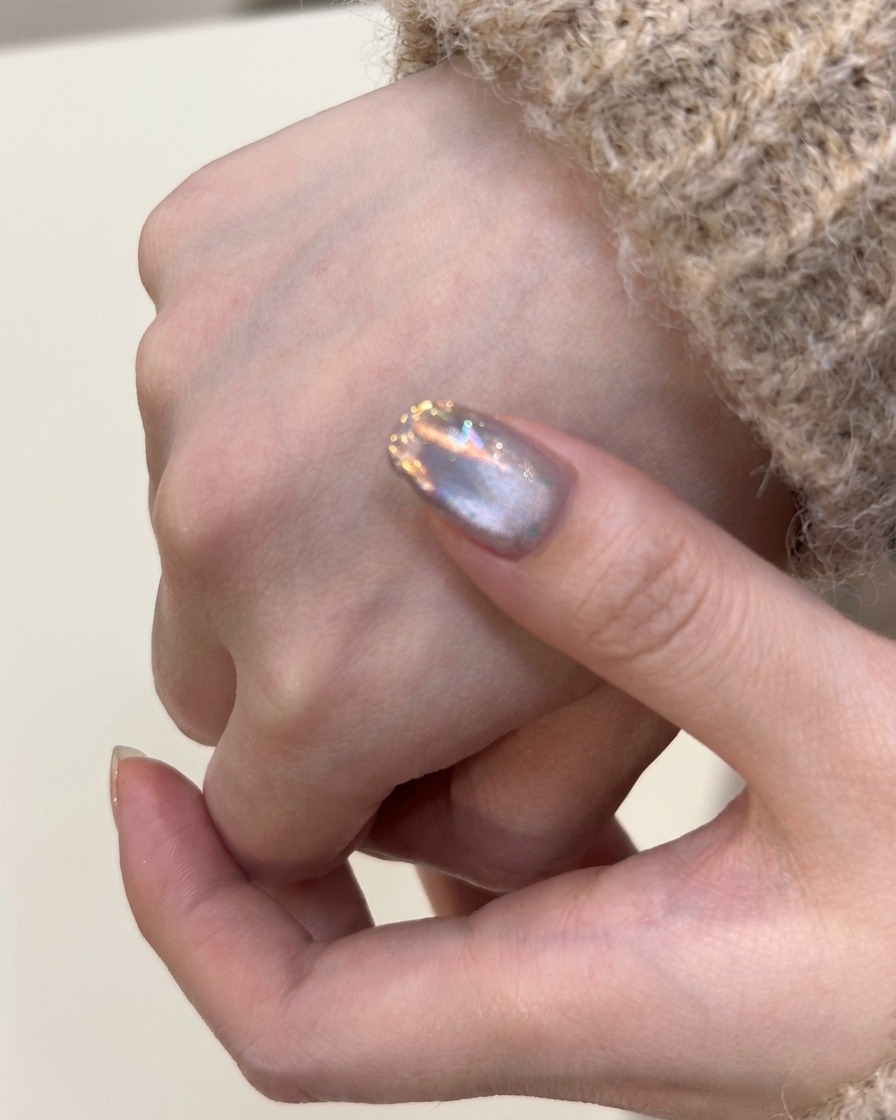 Un pincel aplicando una capa de esmalte de gel ojo de gato plateado sobre una uña natural.