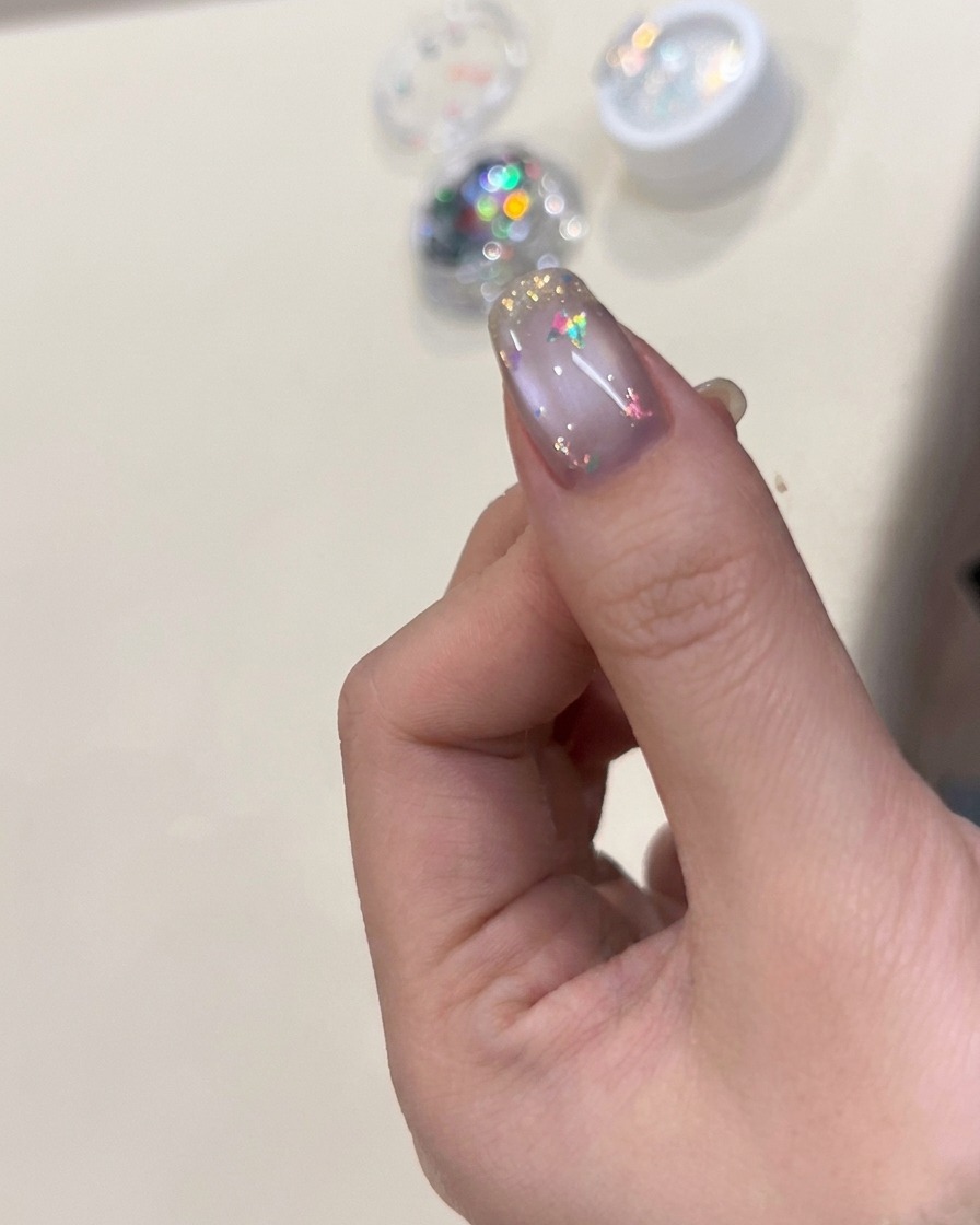 Un pincel de uñas aplicando un top coat transparente brillante sobre una uña decorada con copos y un dije de mariposa.