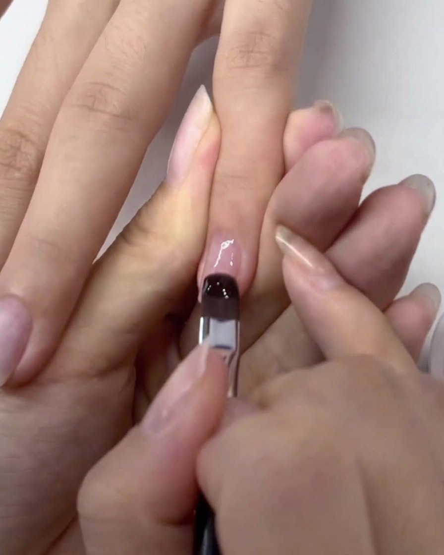 Pincel aplicando una capa transparente de base de gel sobre una uña natural ya preparada.