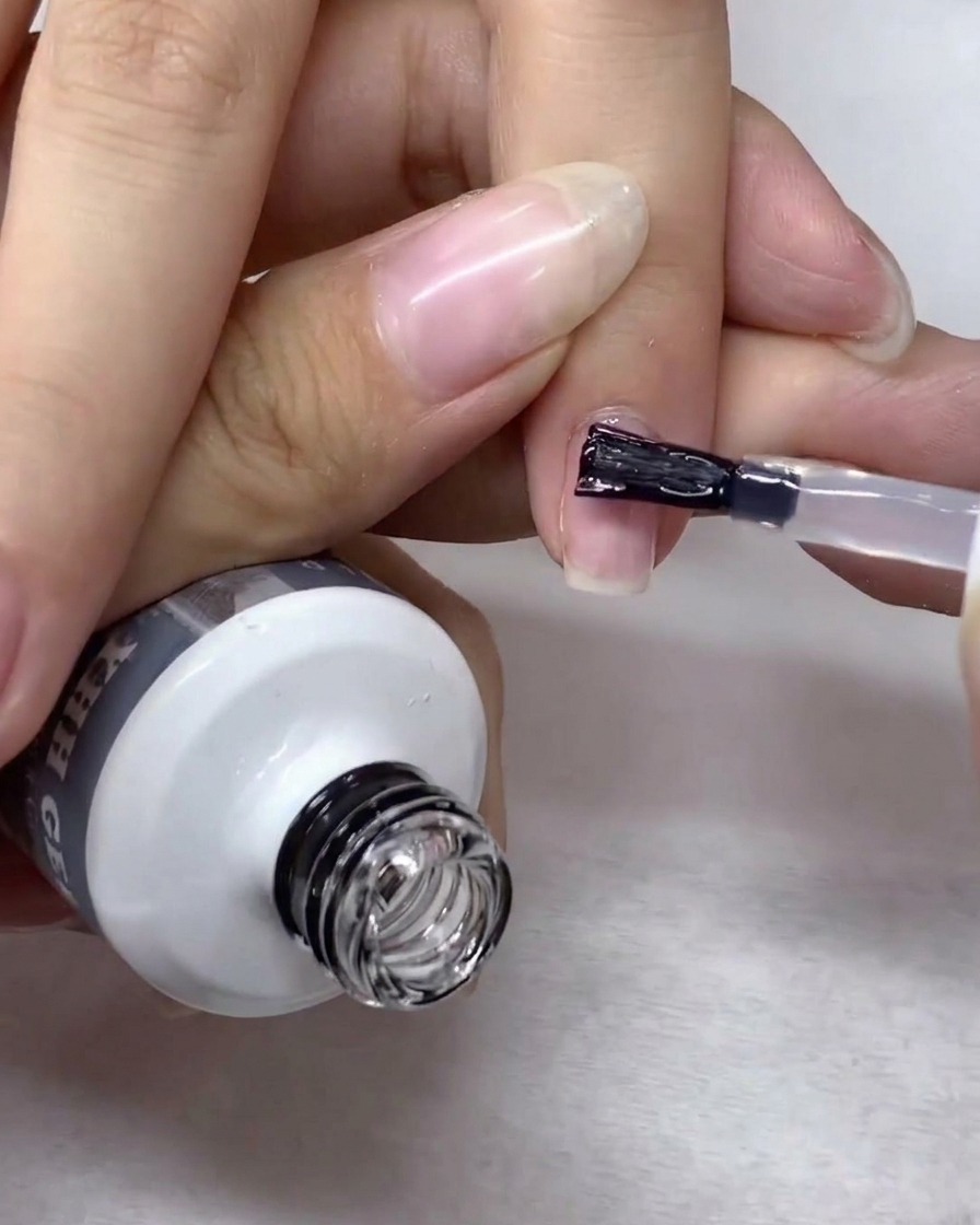 Pincel de nail art esparciendo y alisando suavemente el gel de construcción transparente por toda la superficie de la uña.