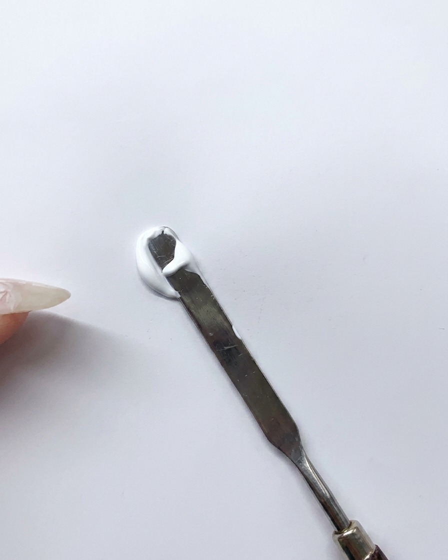 Espátula de metal mezclando gel blanco y azul sobre una paleta limpia para crear un tono azul claro personalizado.