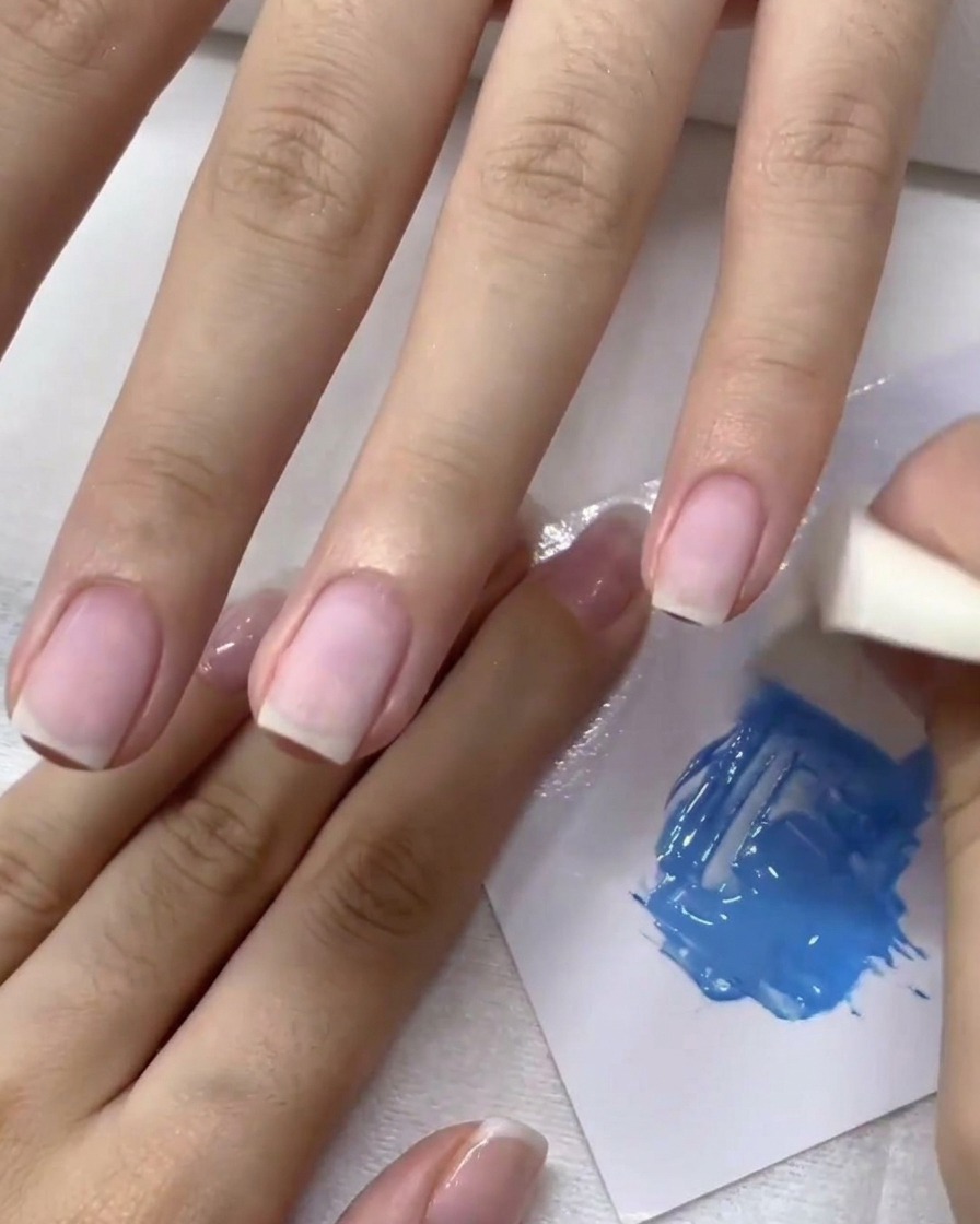 Esponja de maquillaje aplicando gel azul a toquecitos sobre la uña para crear un efecto ombré.