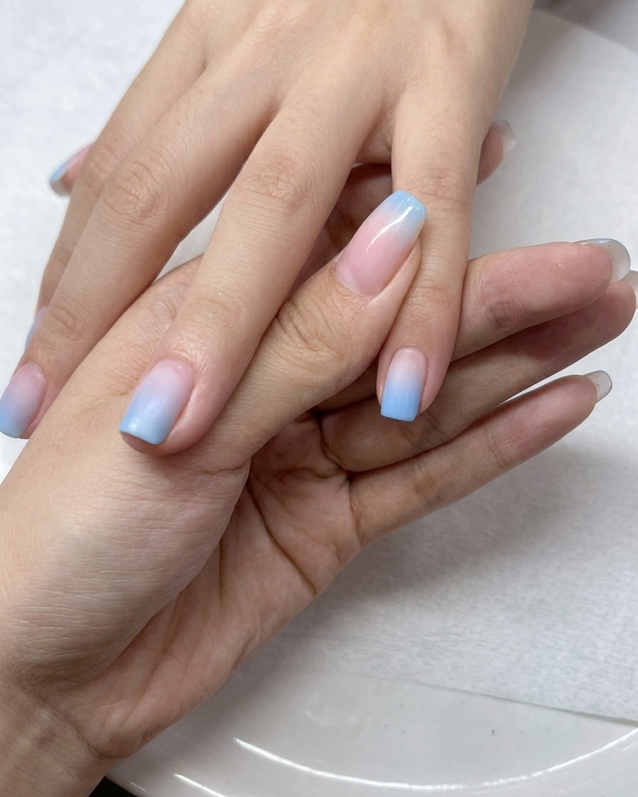 Pincel aplicando una capa de top coat de gel transparente sobre las uñas con degradado ombré.