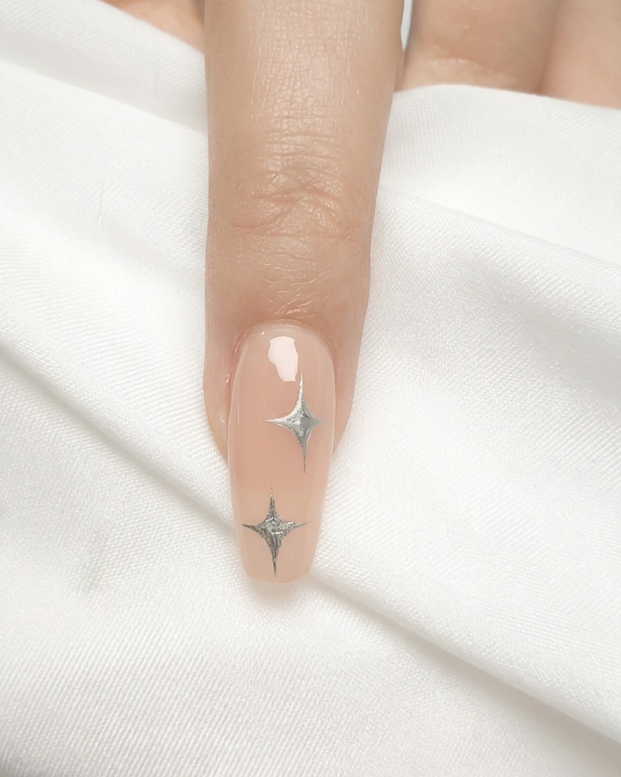 Un pincel de uñas aplicando una capa fina de esmalte de gel nude sobre una uña natural.