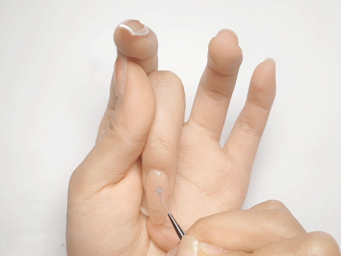 Un pincel de nail art rellenando las esquinas en forma de diamante de una estrella plateada metálica sobre una uña nude.