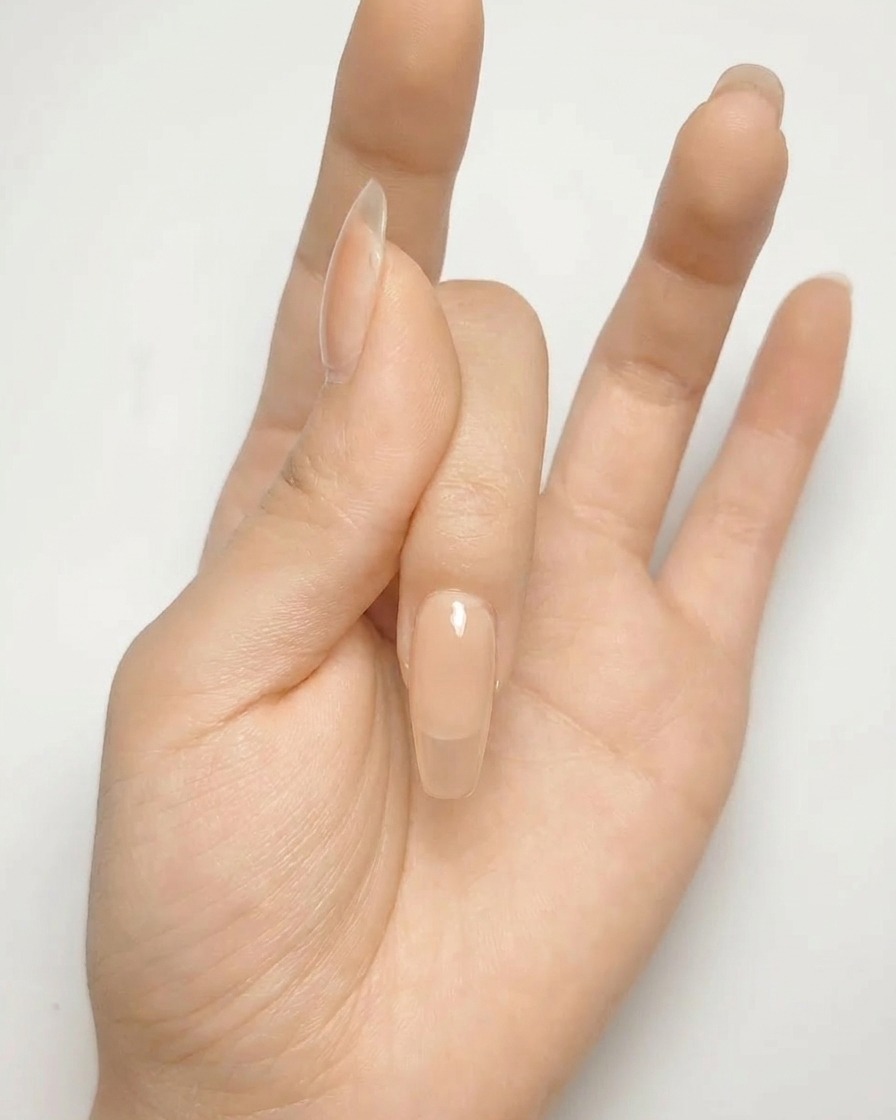 Primer plano de una uña de gel nude con una forma de cruz plateada pintada en la superficie.