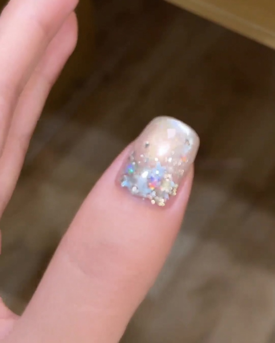Un pincel aplicando una capa de esmalte de gel metálico cat-eye sobre una uña pintada de blanco.