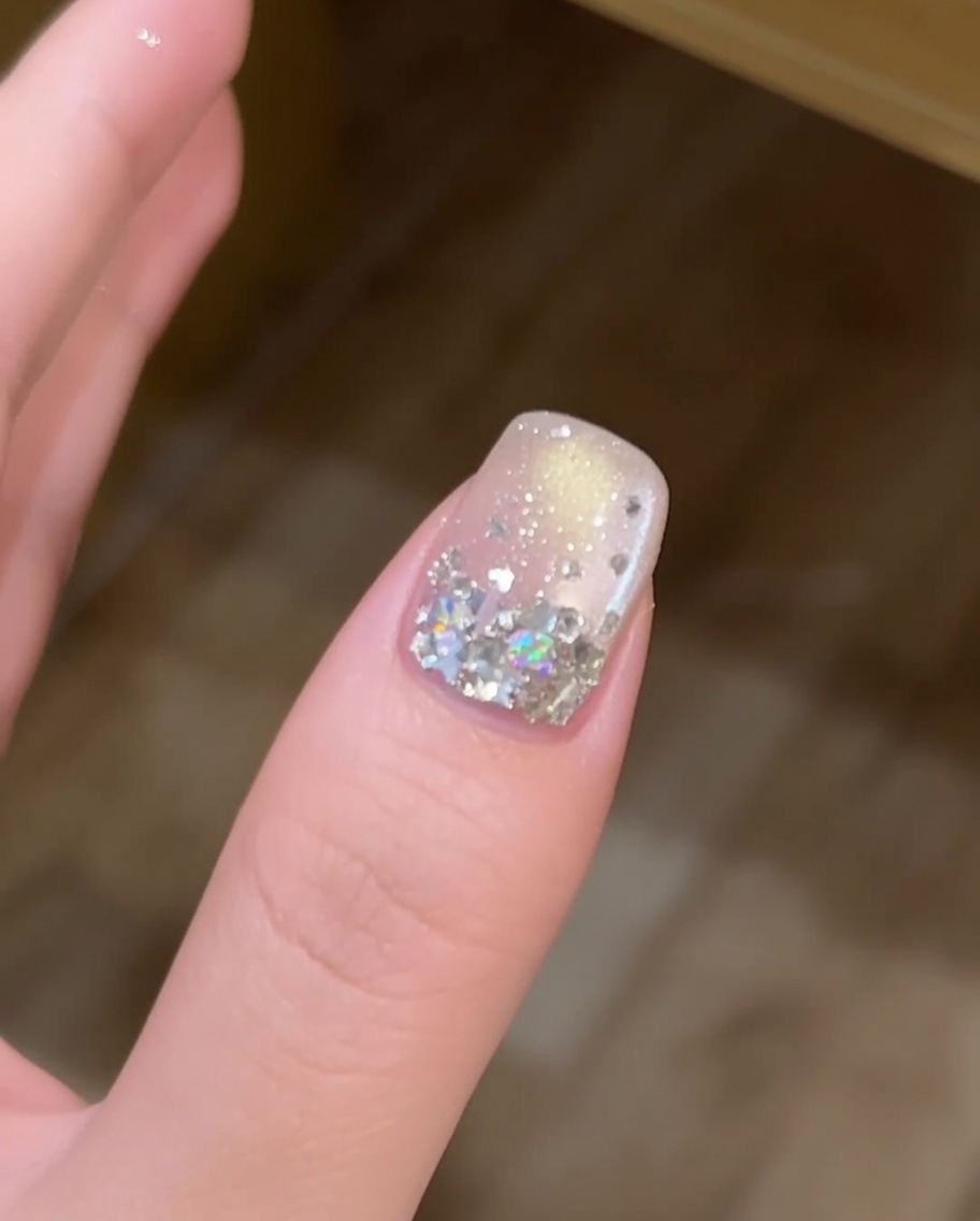Una capa fina de gel constructor transparente siendo aplicada con un pincel sobre una uña decorada con lentejuelas de estrella.
