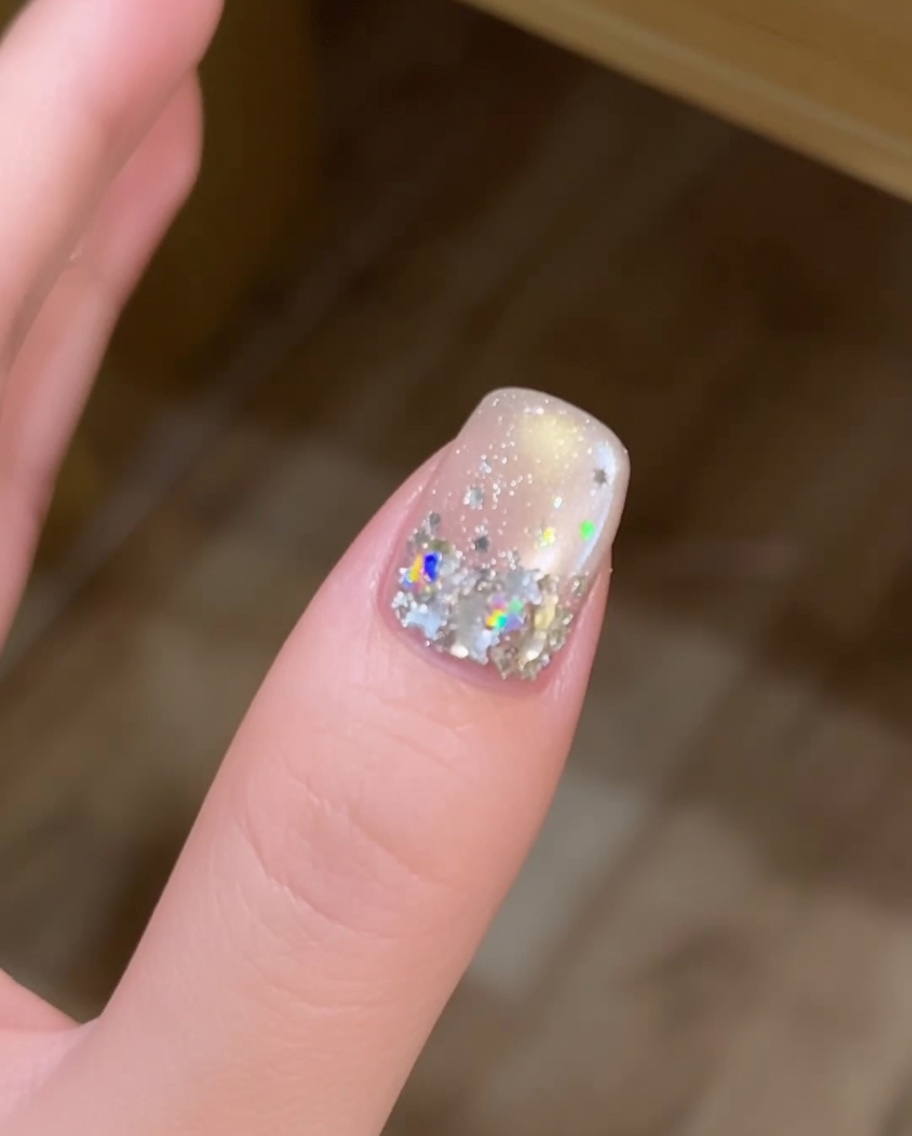 Un pincel de uñas largo aplicando una gota fresca y redondeada de gel constructor transparente en el centro de una uña.