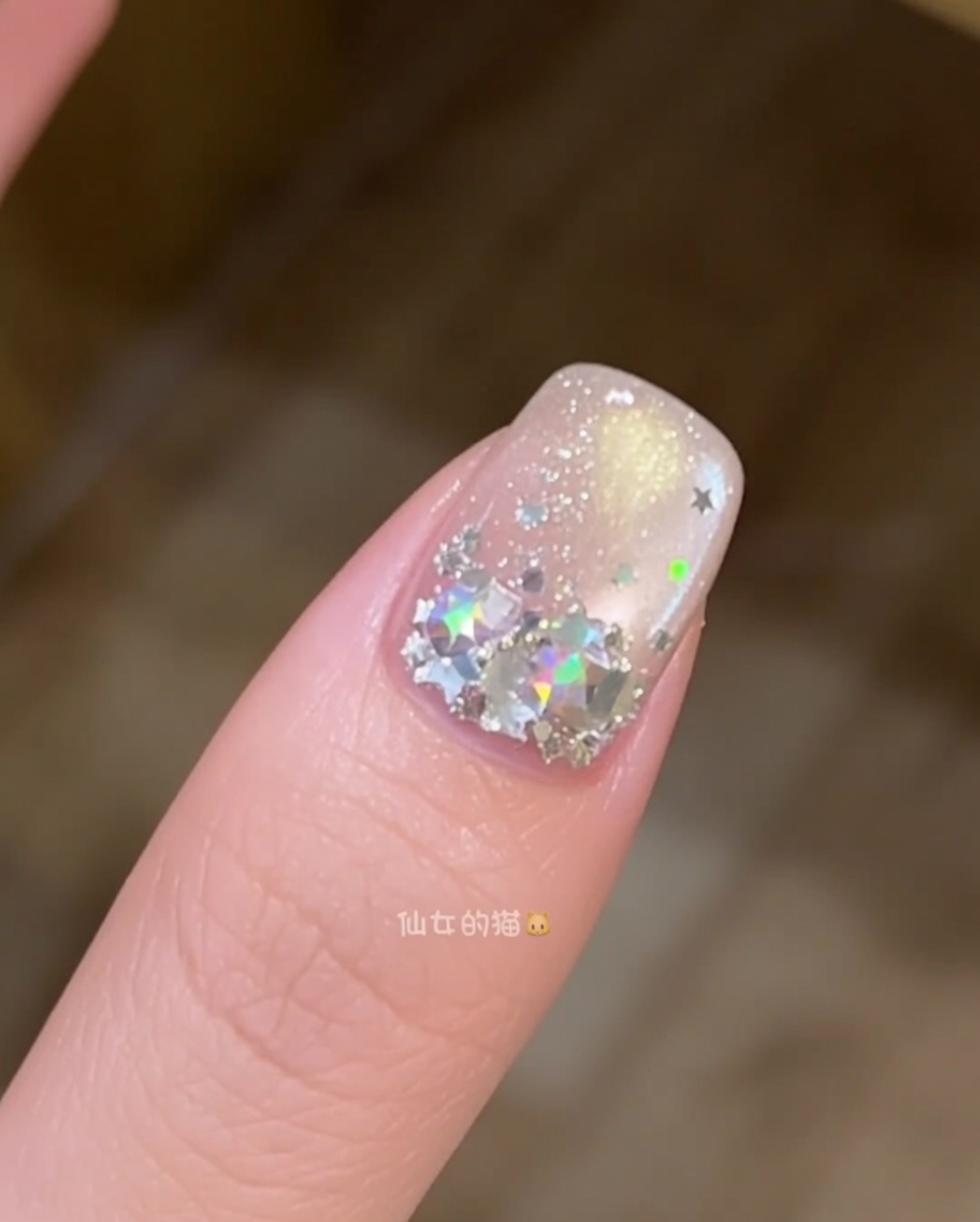 Primer plano de un pincel de uñas alisando una capa de gel constructor transparente en una uña decorada con estrellas.