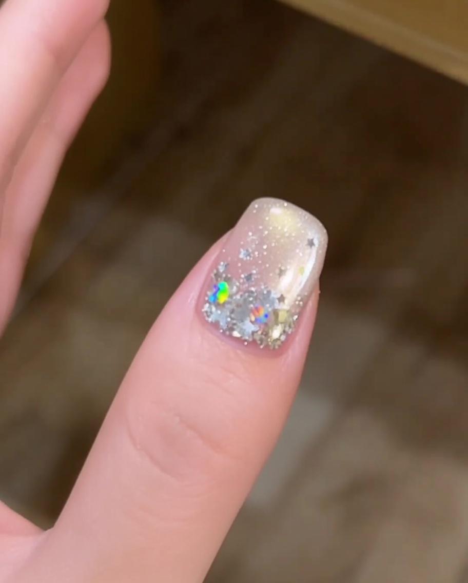 Primer plano de una mano con uñas decoradas con estrellas descansando dentro de una lámpara UV para el curado.