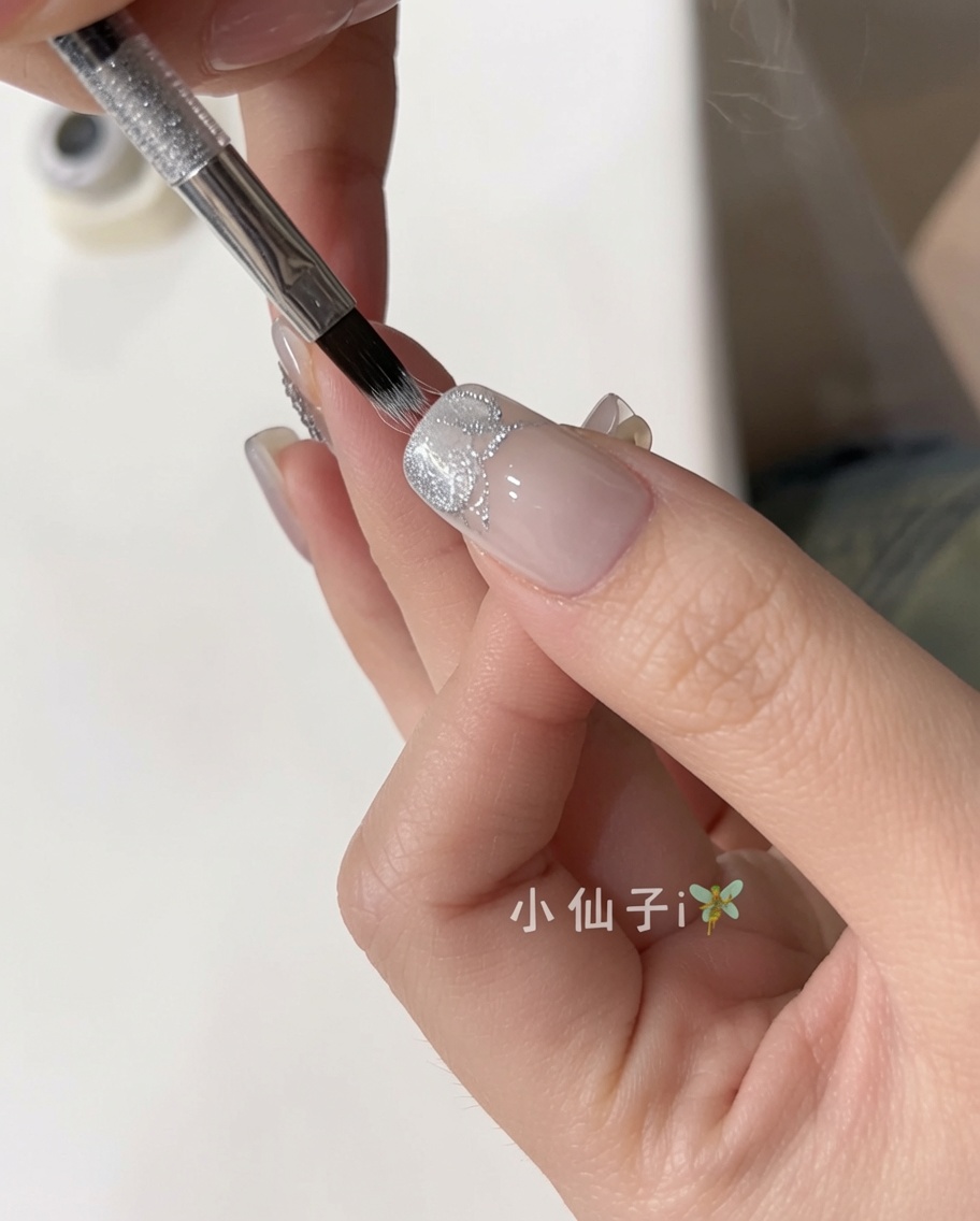 Un pincel aplicando un esmalte gel cat eye plateado brillante sobre una uña natural preparada.