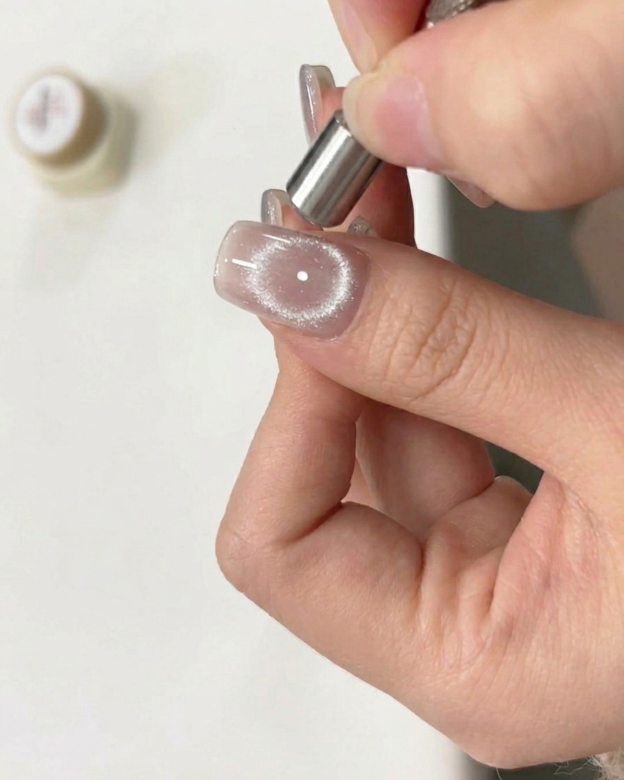 Una herramienta magnética siendo movida en un movimiento circular sobre una uña con gel cat eye húmedo para crear un efecto de anillo.