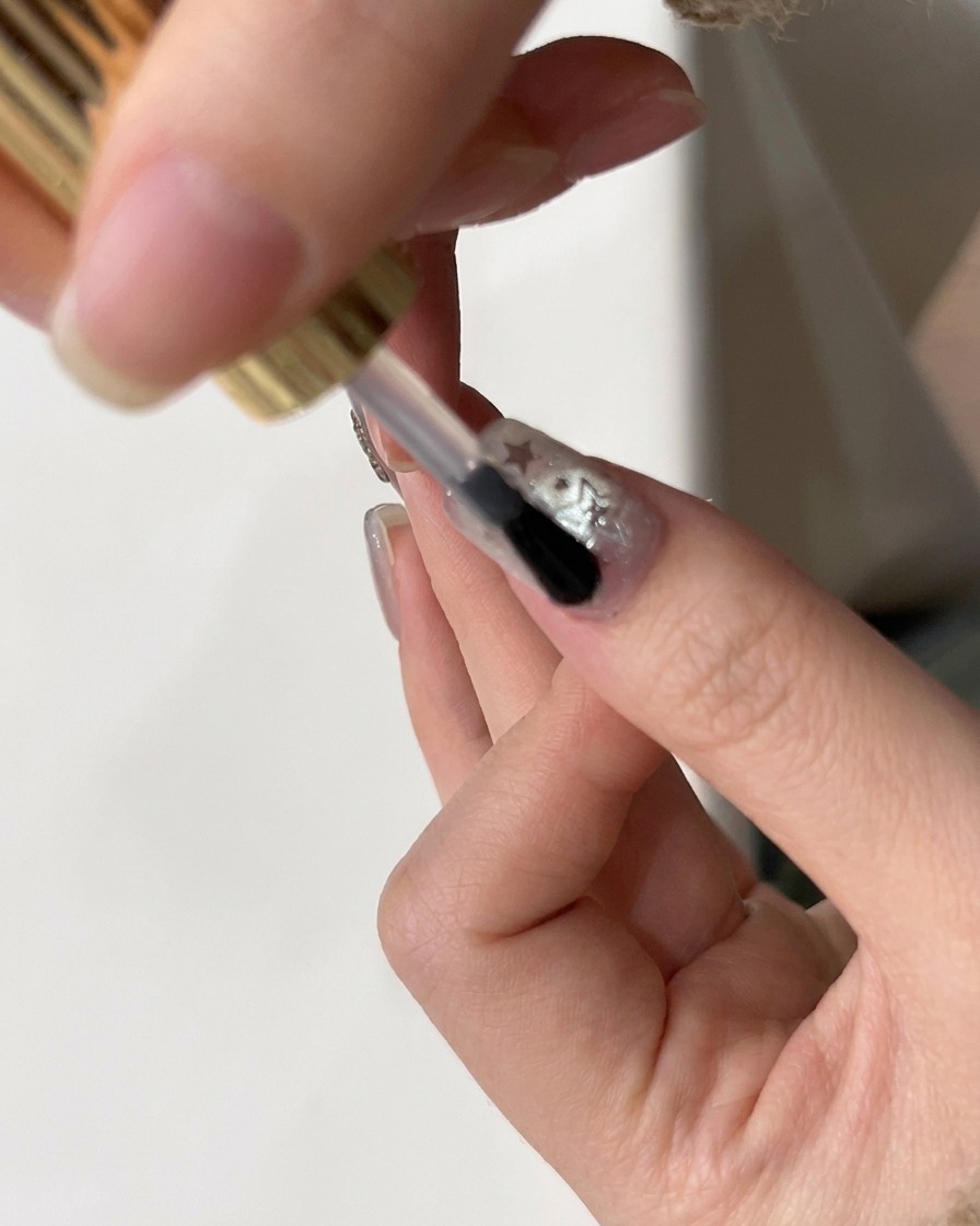 Un pincel aplicando un top coat brillante final sobre una uña decorada con glitter de estrellas.