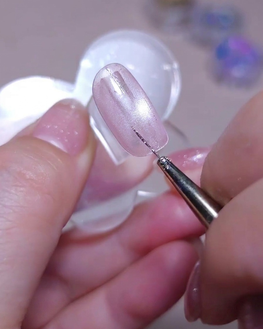 Un pincel liner dibujando una segunda línea vertical de glitter plateado junto a otra existente sobre una uña brillante ojo de gato rosa.