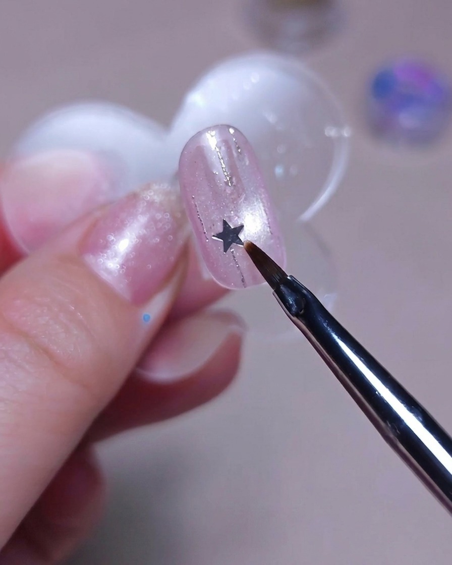 Un pincel fino colocando una pequeña lentejuela plateada en forma de estrella sobre una uña.