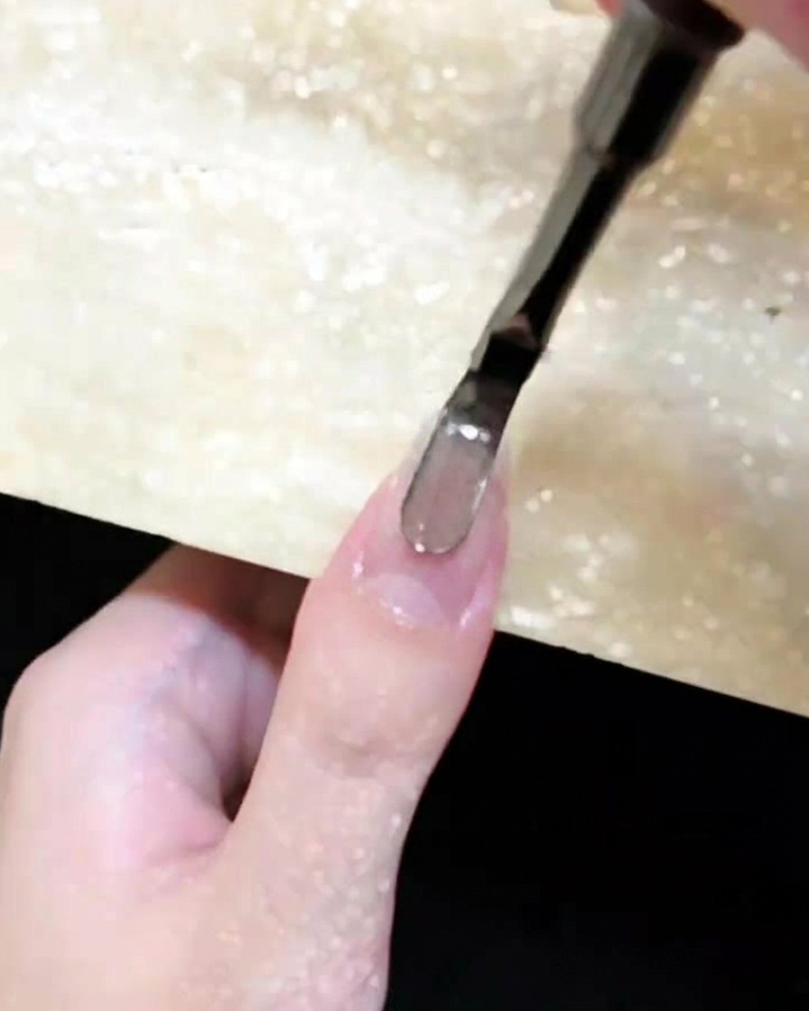 Un pincel de uñas aplicando gel cat eye marrón sobre una uña natural.